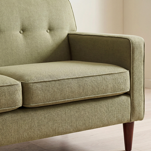 Close-up of a green tufted sofa arm and tapered wood leg