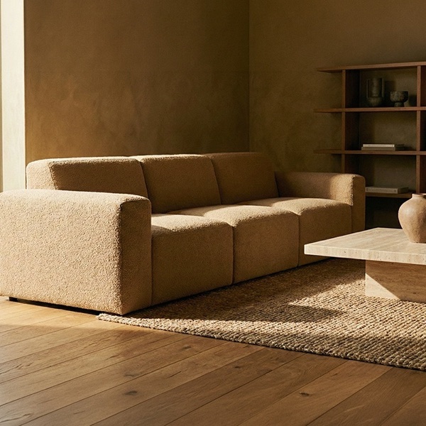 Tan boucle sofa in a warm living room, with a stone table and woven rug